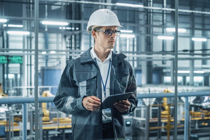 Mann mit Helm und Tablet in Produktionshalle