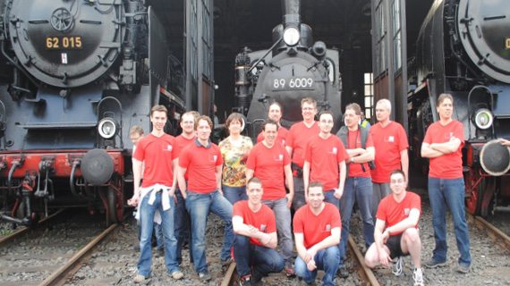 Personengruppe mit roten Shirts vor mehreren Lokomotiven