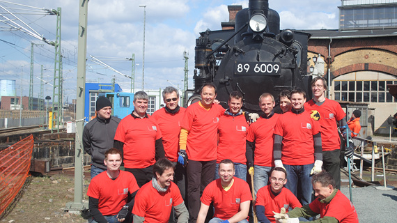 Personengruppe mit roten Shirts stehen vor einer Lokomotive