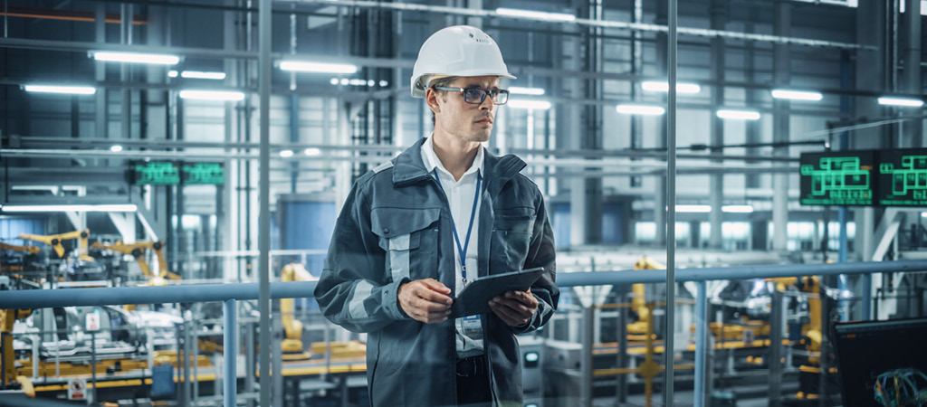 Mann mit Helm und Tablet in Produktionshalle